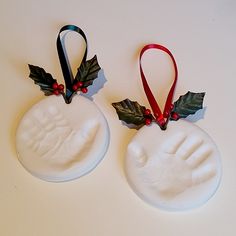 two christmas ornaments made to look like hand and foot prints with holly leaves on them