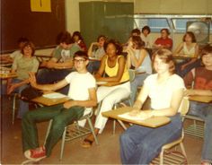 a group of young people sitting at desks in a classroom with one person raising his hand