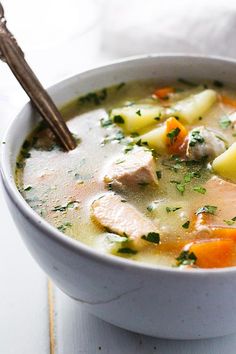 a white bowl filled with chicken and vegetable soup on top of a wooden cutting board