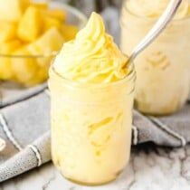 a jar filled with yellow whipped cream next to some pineapples