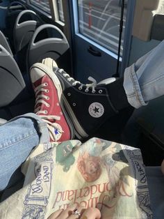 two people sitting on a bus with their feet up and one person holding a book