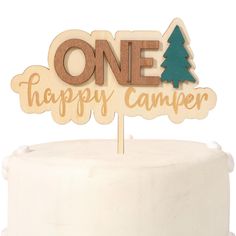 a one happy camper wooden sign on top of a white cake with pine trees