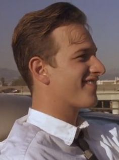 a young man wearing a white shirt and black tie sitting in a car looking off into the distance