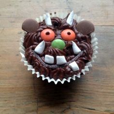 a cupcake with chocolate frosting and decorations on it's face is sitting on a wooden table