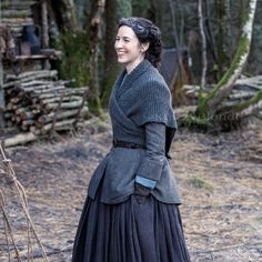 a woman in a long black dress is walking through the woods with her hand on her hip