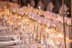 the table is set with candles and pink roses in glass vases on each side