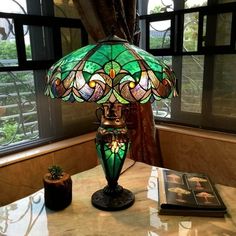 a green lamp sitting on top of a table next to a book and potted plant