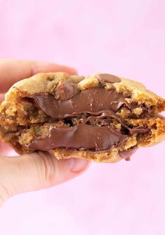 a hand holding a chocolate chip cookie with one bite taken out and the other half eaten