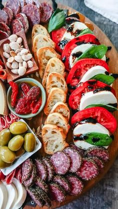 an assortment of meats and cheeses on a wooden platter with olives