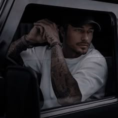 a man with tattoos sitting in the passenger seat of a car looking out the window