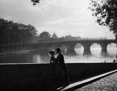 an old photo of two people standing by the water