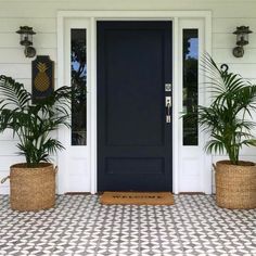 two planters on the front porch of a white house with black door and windows