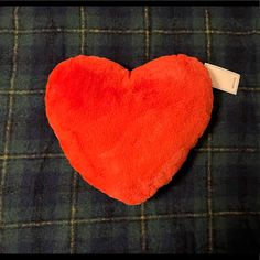 a red heart shaped pillow sitting on top of a plaid table cloth with a tag attached to it