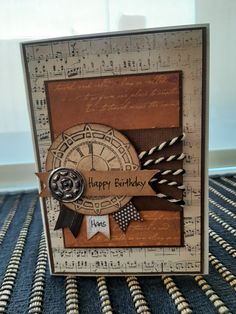 a happy birthday card with music notes and a clock on the front, sitting on a table