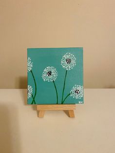 a small easel with a painting of white flowers on it sitting on a table