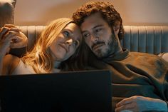 a man and woman laying on a couch looking at a laptop computer screen while they look at each other