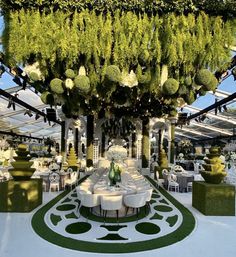 an outdoor dining area with white tables and green plants on the ceiling, surrounded by greenery