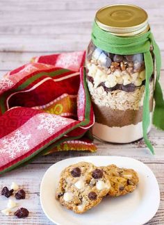 two cookies are sitting on a plate next to a jar with chocolate chips and marshmallows