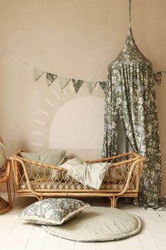 a wicker day bed with pillows on the floor in front of a curtained window