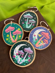 three hand painted wooden hoops with mushrooms and flowers on them sitting on a table