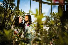 a man and woman standing next to each other in front of plants