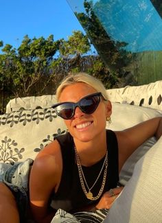 a woman laying on top of a white couch wearing sunglasses and smiling at the camera