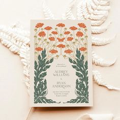 an orange and green floral wedding card on top of a white tablecloth with leaves