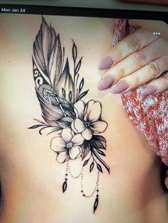 a woman's stomach with a feather and flowers tattoo on it, next to her hand