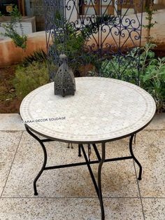 a white table sitting on top of a tiled floor next to a planter and fence