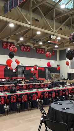 tables and chairs are set up in the gym for a football themed party with red, white and black balloons