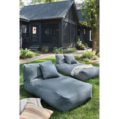 an outdoor lounge chair and ottoman on the grass in front of a house with a black shingled roof