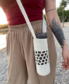 a person holding a cell phone in their hand and wearing a crochet bag