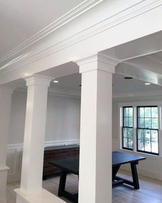 an empty room with white columns and black table in the center, surrounded by wood flooring