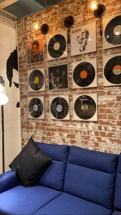 a blue couch sitting in front of a brick wall with records on the wall behind it