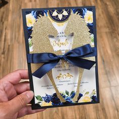 a hand holding up a wedding card with a blue ribbon and gold foil on it