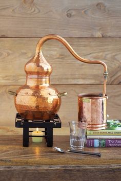 an old fashioned copper kettle with a candle and some books next to it on a wooden table