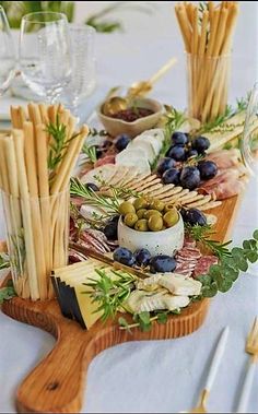 an assortment of cheeses, olives and bread sticks on a wooden platter