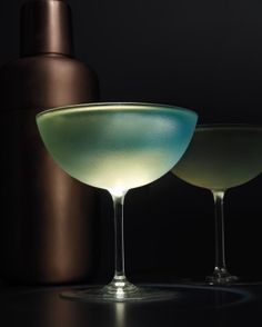 two martini glasses sitting next to each other on top of a black table with a bottle in the background