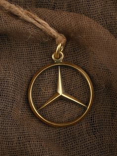 the mercedes logo is shown in gold on a brown fabric background with some jute