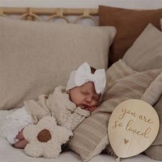 a baby sleeping on top of a bed next to a teddy bear and wooden sign