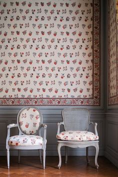 two chairs sitting next to each other in front of a wall with flowers on it