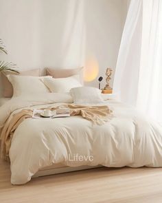 a bed with white sheets and pillows in a room next to a plant on the floor