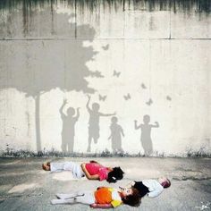 two children are laying on the ground in front of a wall with shadows of people