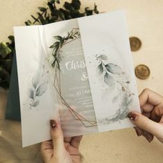 two hands holding an open wedding card with greenery on the front and back side