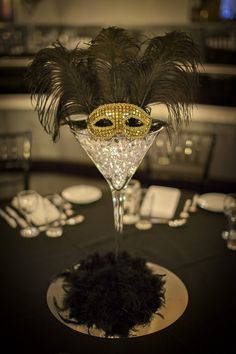 a masquerade mask sitting on top of a martini glass filled with black feathers