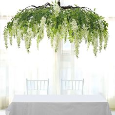 the table is covered with white flowers and greenery hanging from it's ceiling