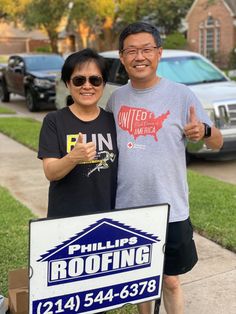 two people standing in front of a roofing sign giving the thumbs up and smiling