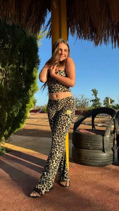 a woman in leopard print pants standing under a thatched umbrella with her hands on her hips