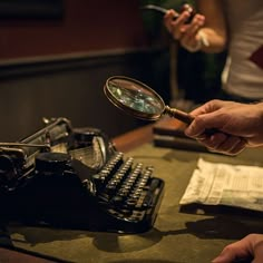 a person holding a magnifying glass next to an old typewriter on a table