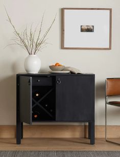 a black cabinet with a white vase and oranges on it next to a chair